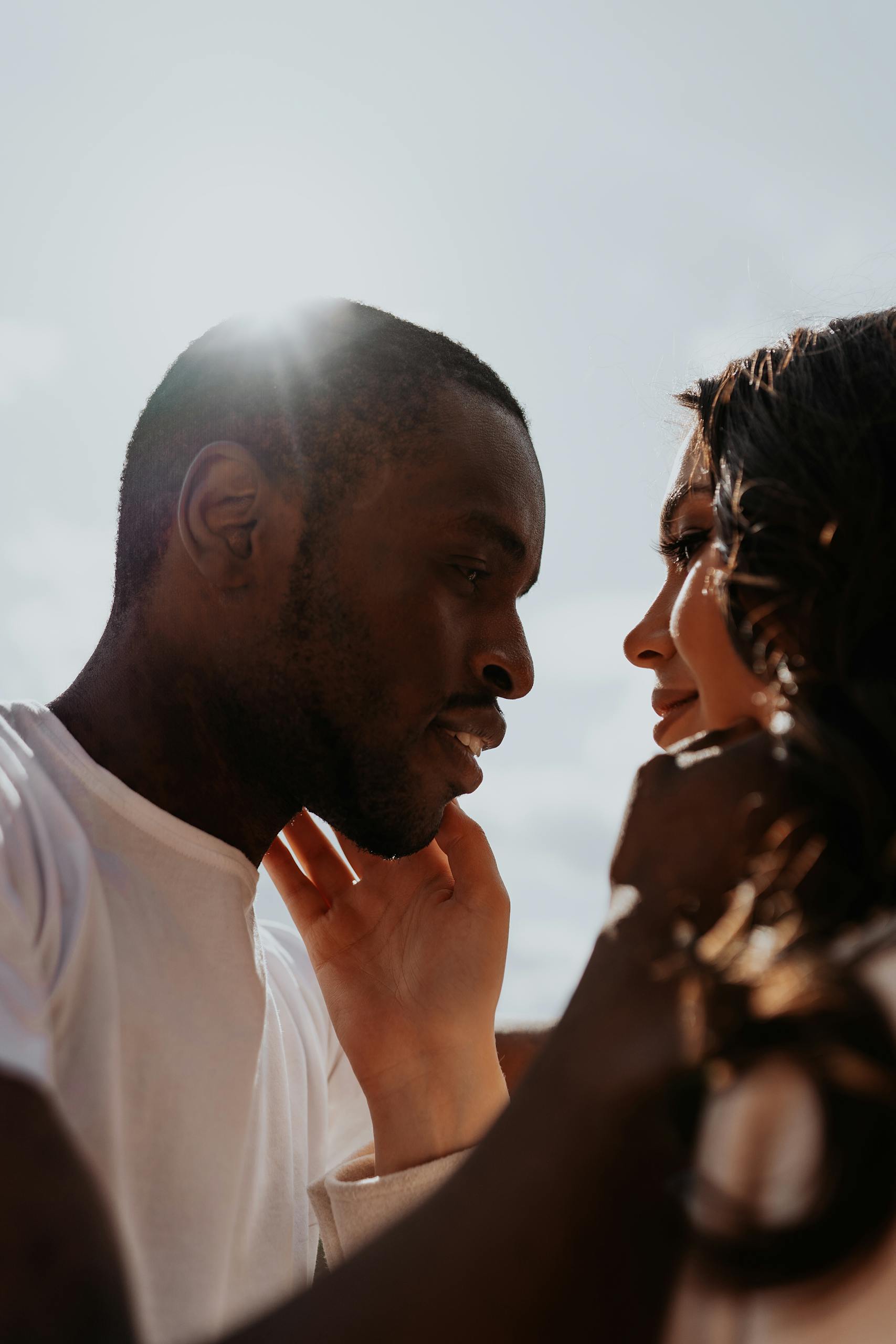A close-up shot of an interracial couple sharing an affectionate moment outdoors in the sun.