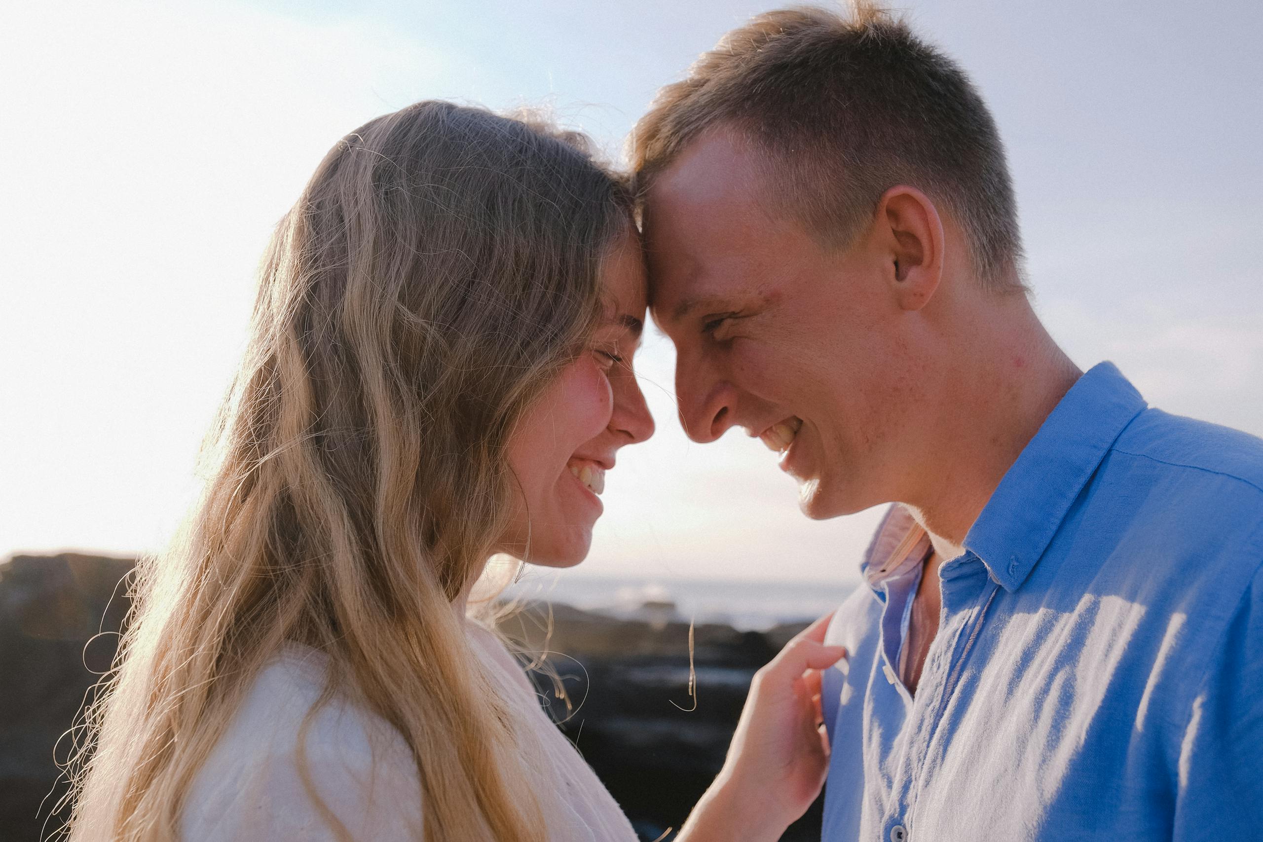 A loving couple shares a joyful moment outdoors, dressed casually under a sunny sky.