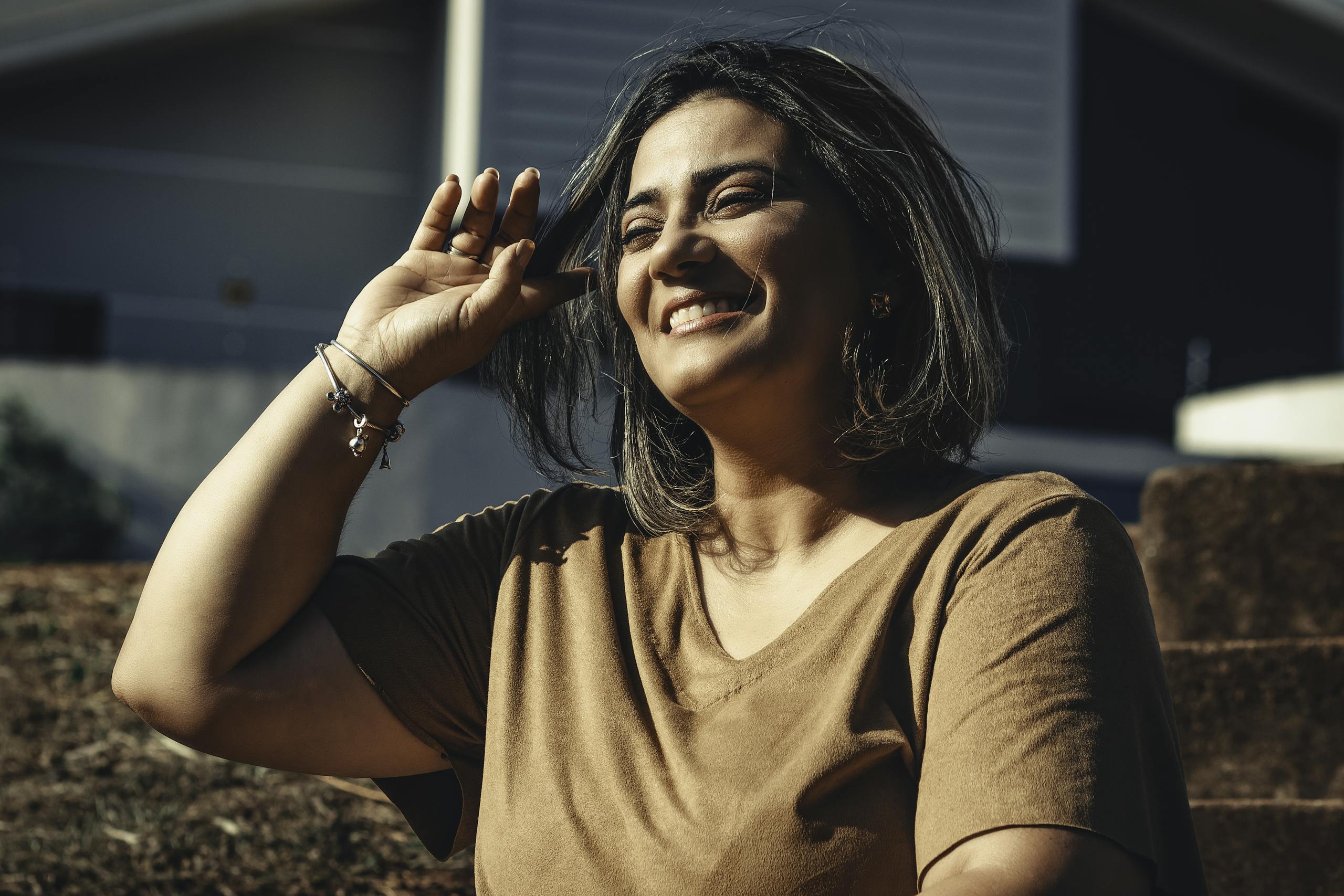 A woman smiling joyfully while sitting outside in natural sunlight.