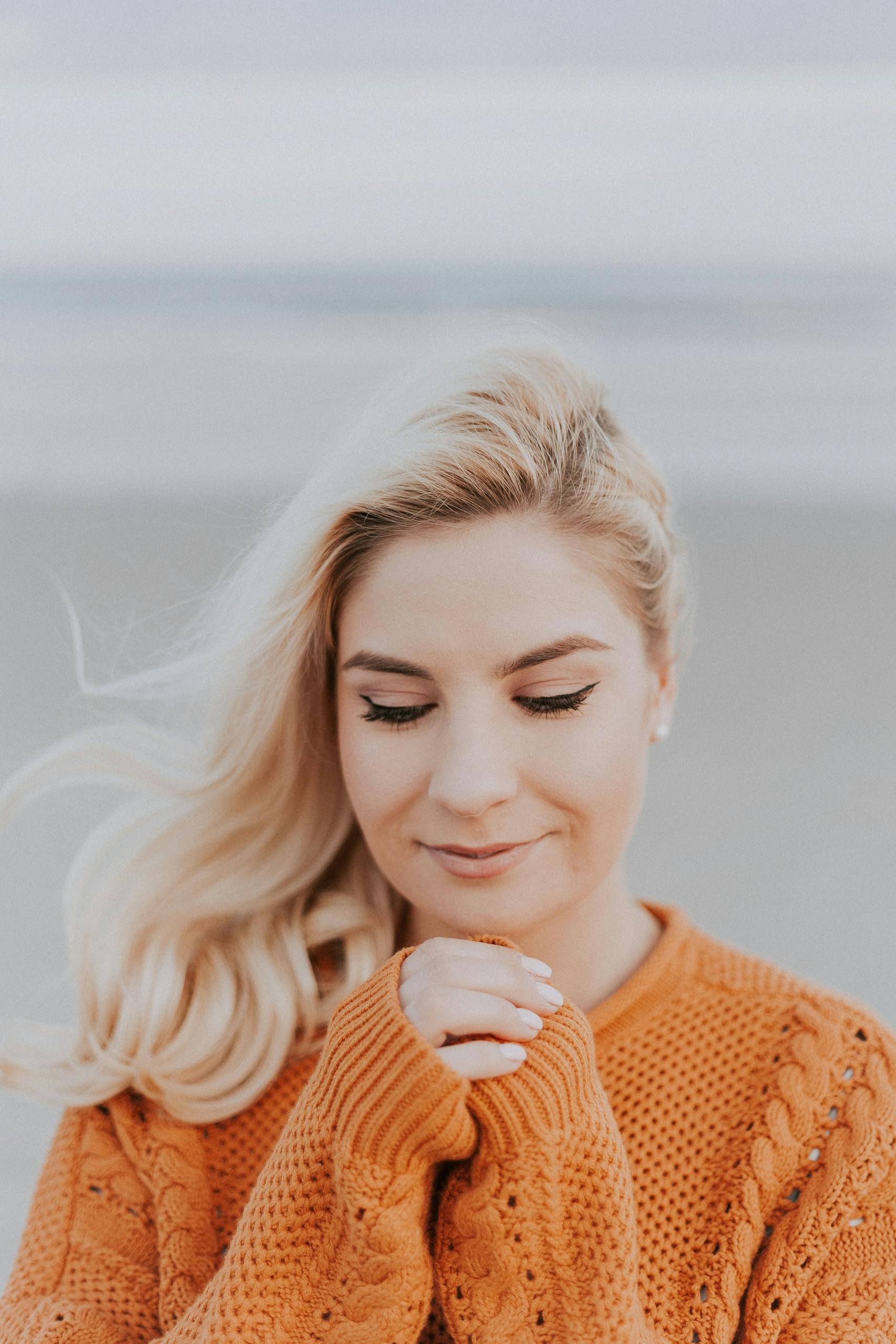 Blonde woman in knitted sweater enjoying a peaceful moment on a windy beach.