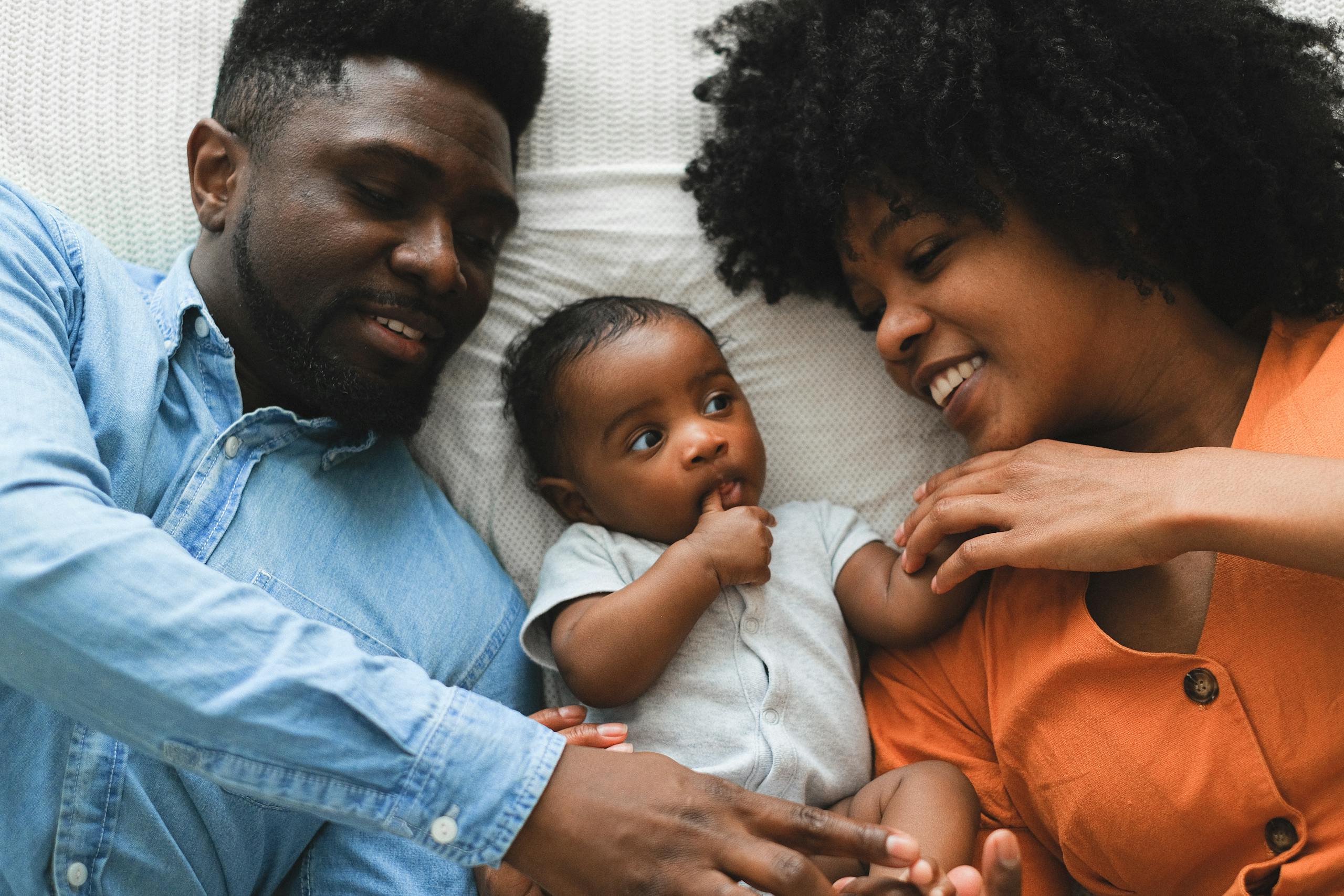 Smiling parents and baby bonding together on a bed, showcasing love and joy.