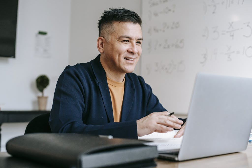 Smiling professional man engaged in remote work using a laptop in a modern office setting.