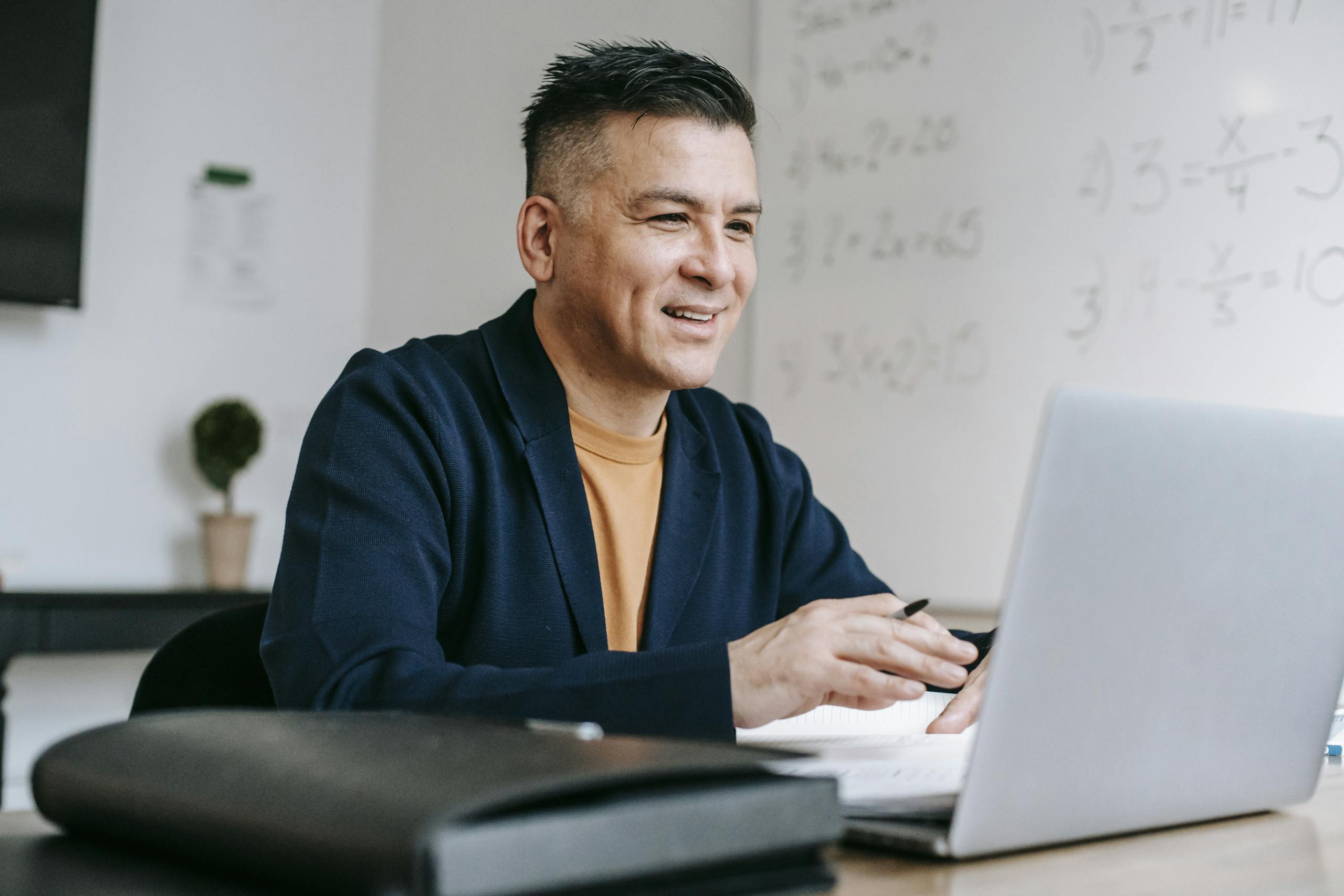 Smiling professional man engaged in remote work using a laptop in a modern office setting.