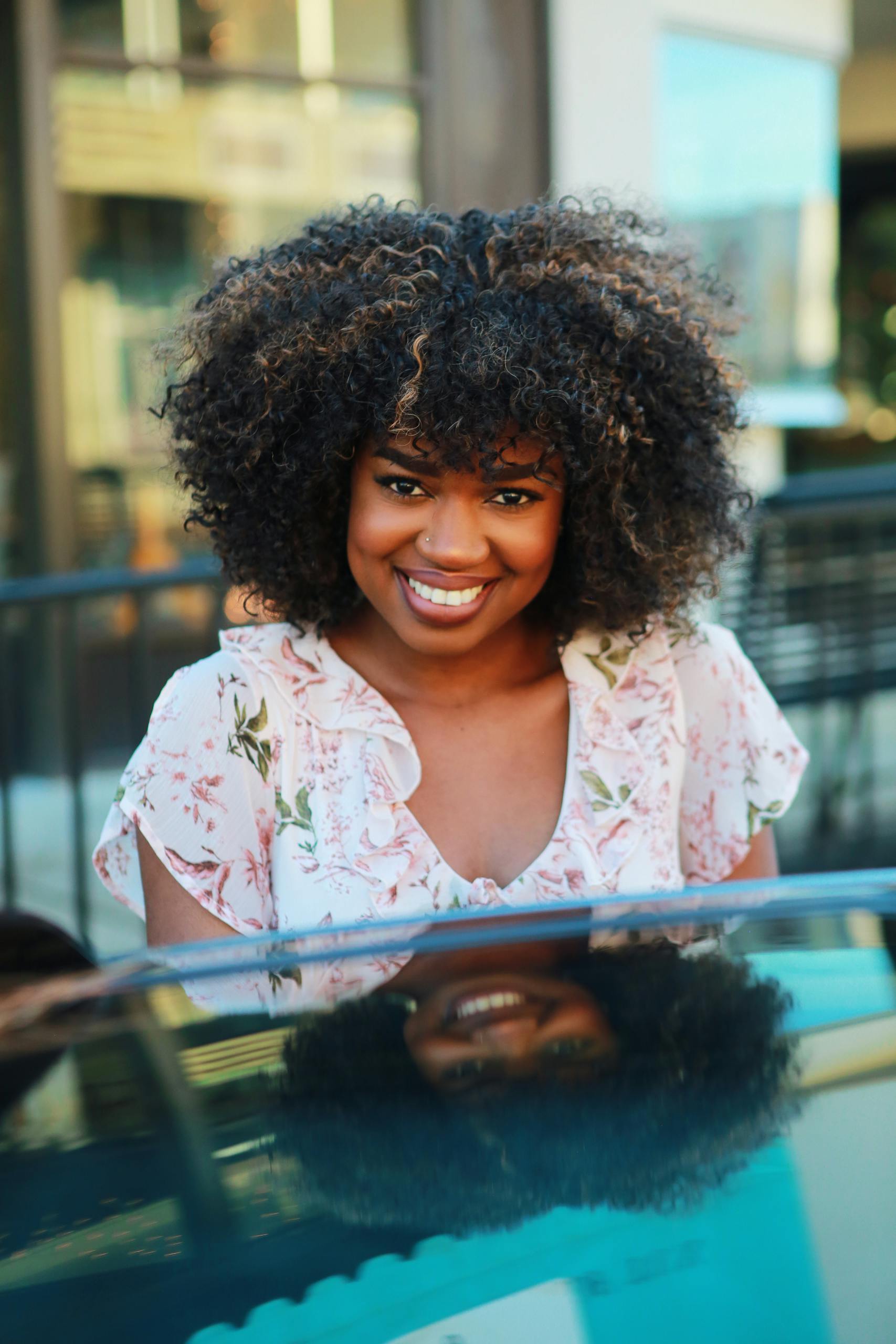 Smiling woman with natural afro hairstyle outdoors in a floral dress, capturing joy on a sunny day.